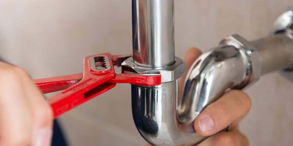 Plumber using a wrench to tighten a nut on a pipe under the sink