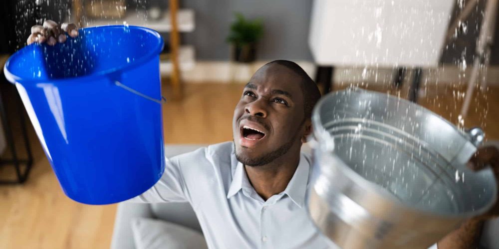 Man holding buckets trying to deal with leaking ceiling