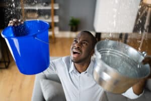 Man holding buckets trying to deal with leaking ceiling