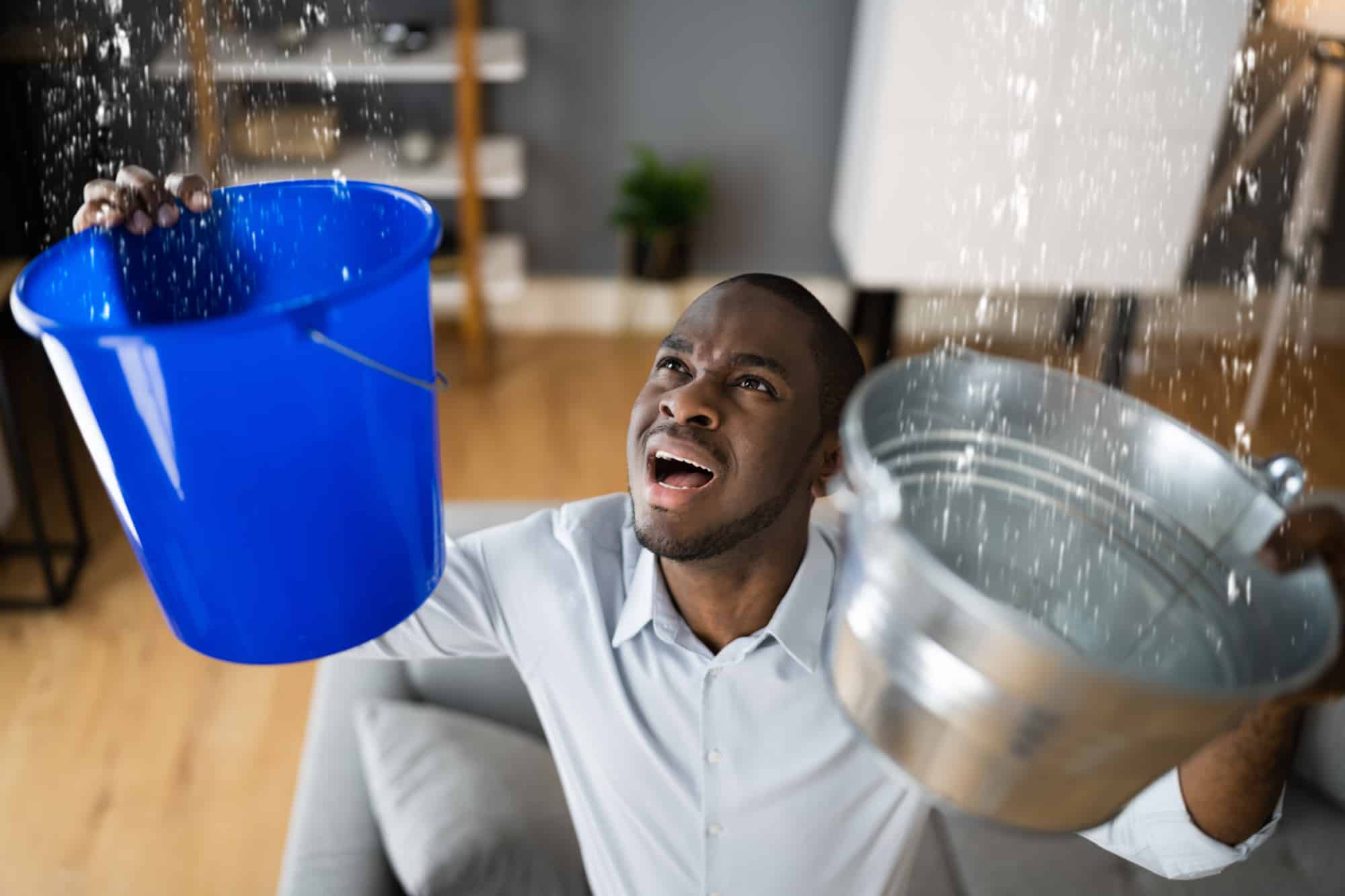 Man holding buckets trying to deal with leaking ceiling